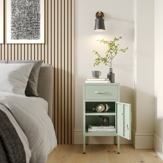 Metal side table locker in sage green with one drawer and one door open showing books, in a room next to a bed