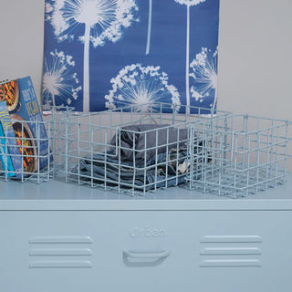 A set of 3 blue baskets containing cook books and jeans, sitting on a blue set of metal drawers